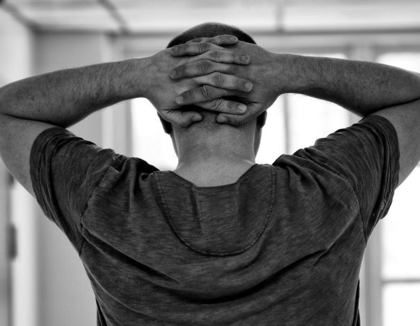 man holding arms behind head in black and white