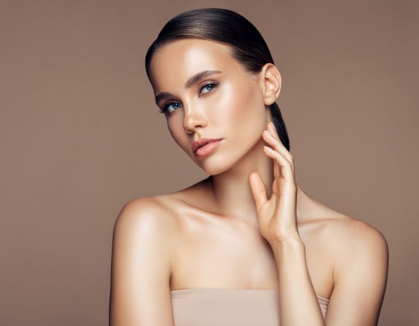 Brunette woman on a tan background looking at the camera with her hand on her chin after getting Morpheus8 Treatment